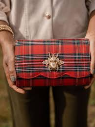 Red and black plaid clutch with a bee emblem held by a person wearing a gray suit.