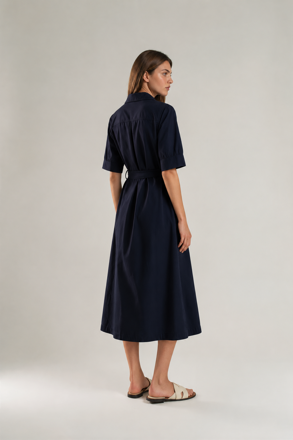 A woman modeling a dark navy midi shirt dress with short sleeves, a button-up front, and a matching self-tie belt.