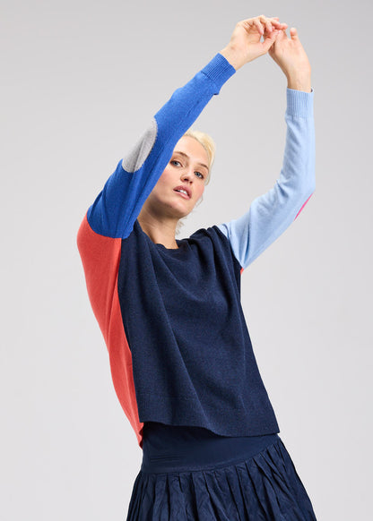 Woman wearing a colorful sweater with blue, red, and navy panels on a gray background