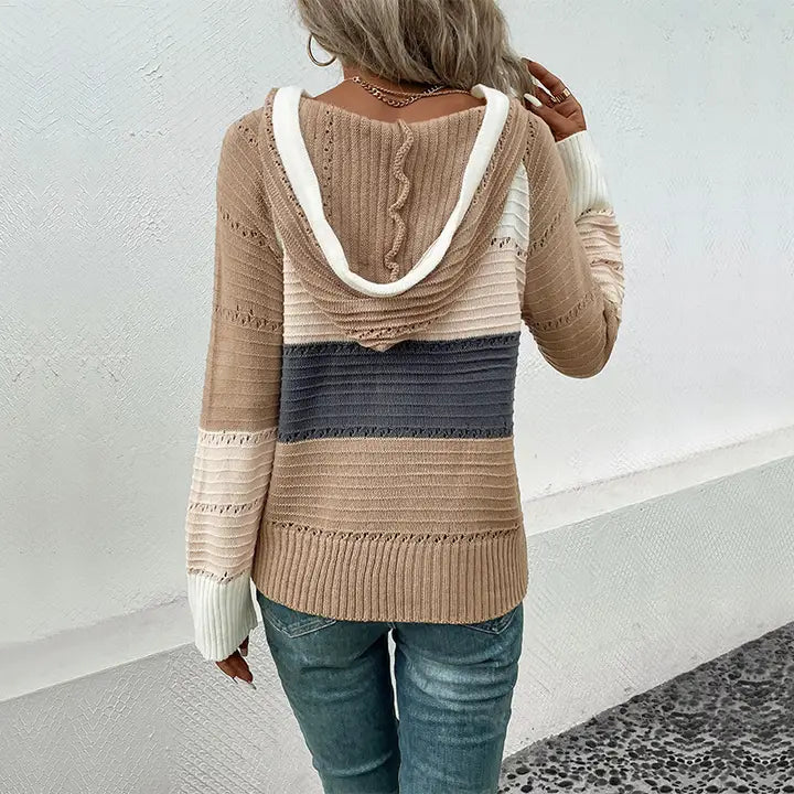 Person wearing a striped sweater with a hood against a white wall