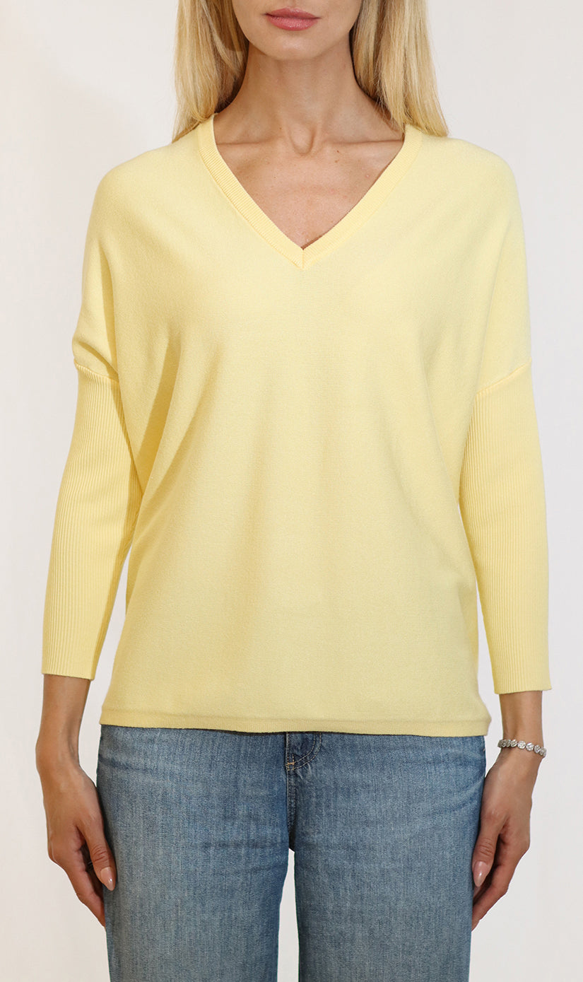 Person wearing a light yellow long-sleeve top and blue jeans on a white background