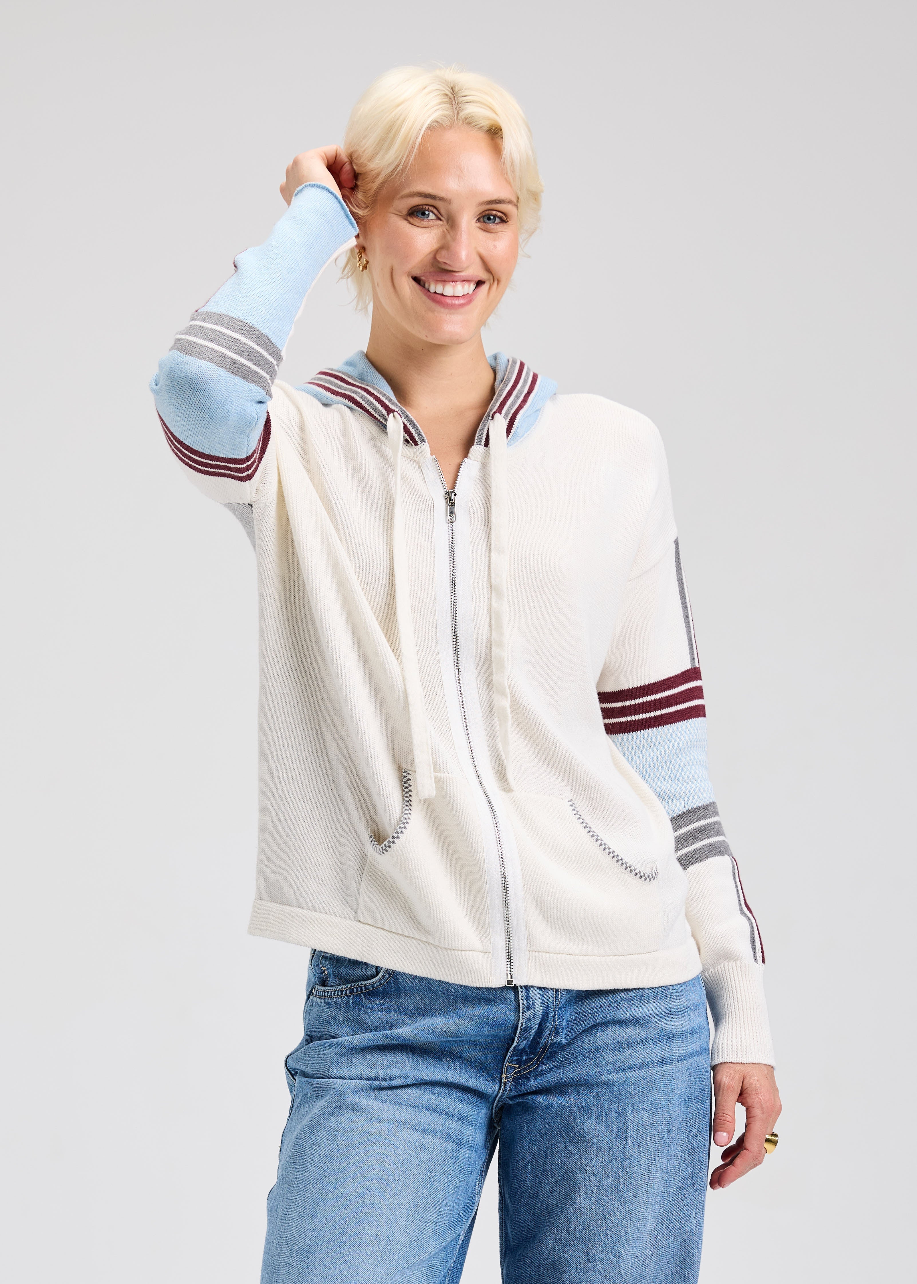 Woman wearing a cream-colored zip-up sweatshirt with colorful sleeves on a light gray background