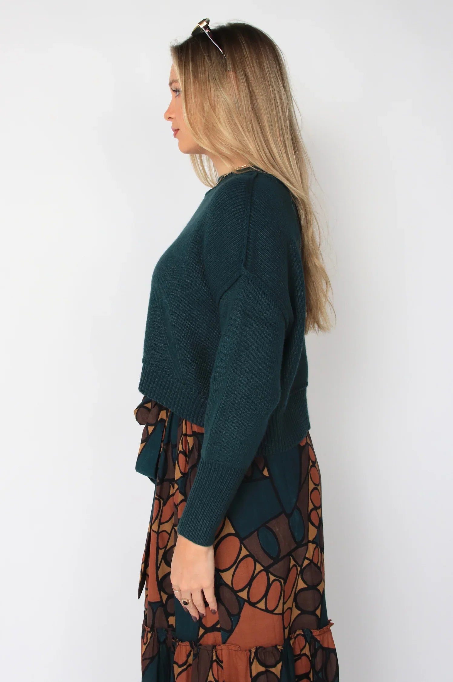 Woman wearing a green sweater and patterned skirt against a white background