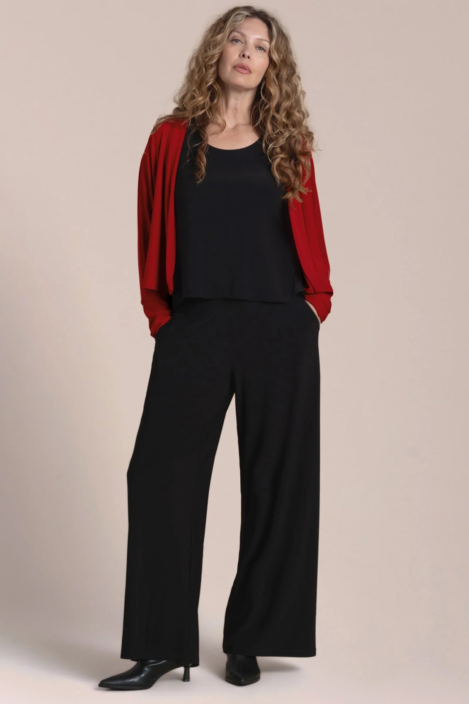 Woman wearing a red jacket, black top, and black pants against a beige background