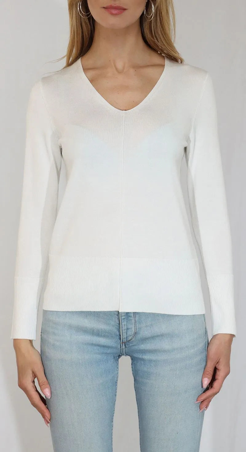 Person wearing a white long-sleeve top and light blue jeans on a plain background