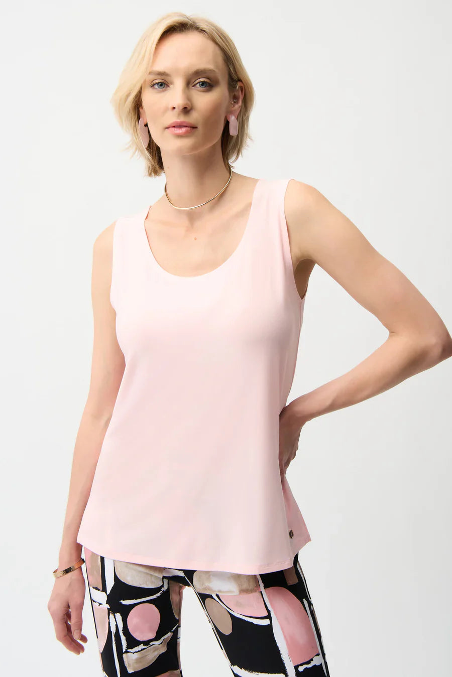 Woman wearing a light pink sleeveless top and patterned leggings on a white background