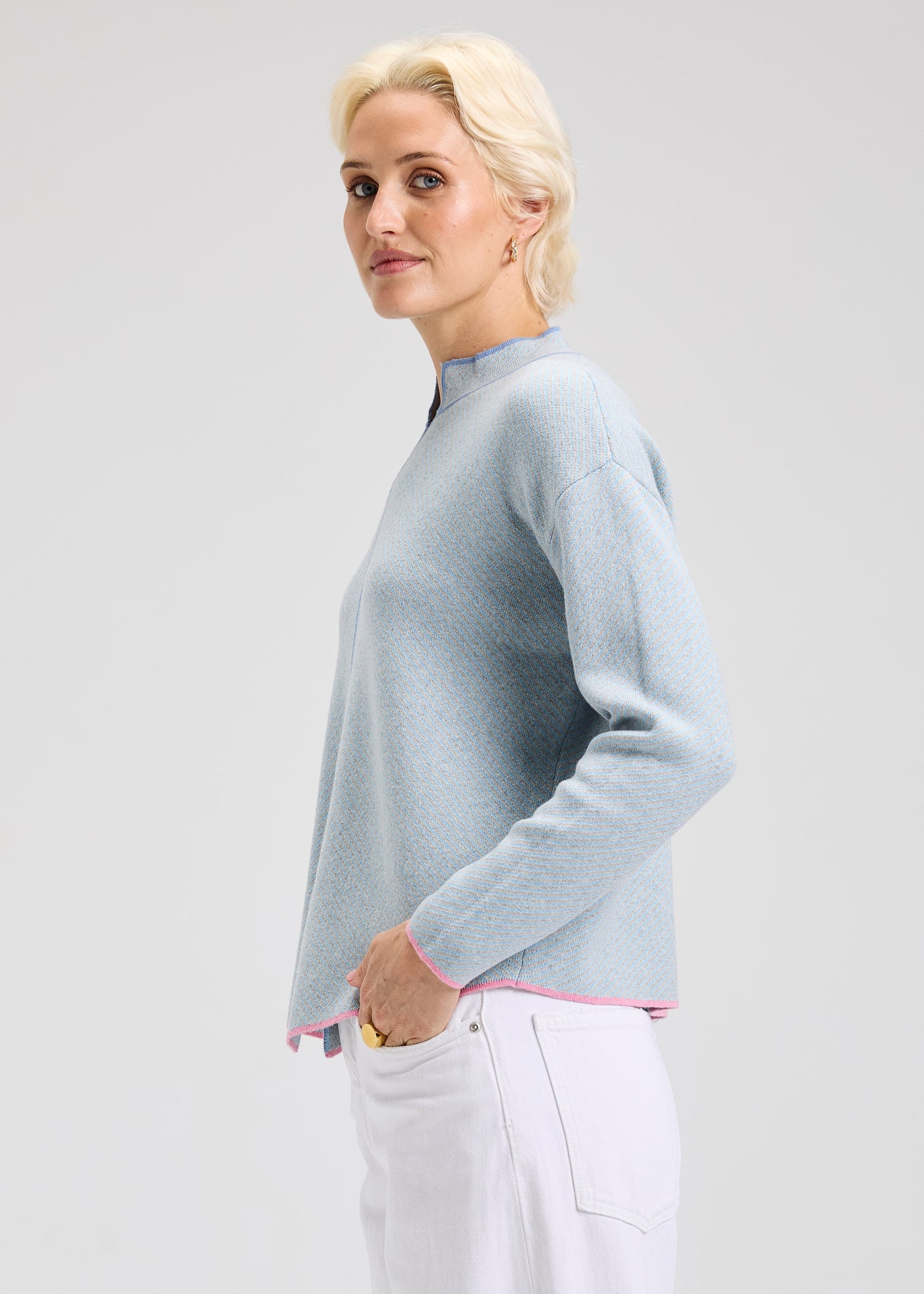 Woman wearing a light blue sweater with dark blue and pink details with a plain background