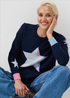 Woman wearing a navy sweater with a large star design, sitting against a plain background.