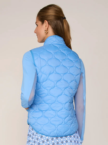 Woman wearing a blue quilted vest against a beige background
