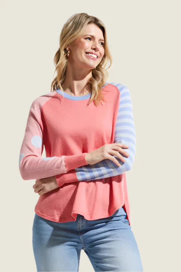 Woman wearing a pink and blue striped long-sleeve top with light blue jeans on a beige background