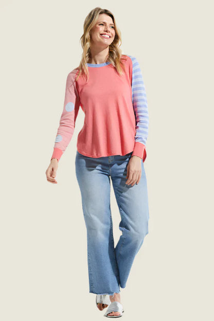 Woman wearing a pink and blue striped long-sleeve top with light blue jeans on a beige background
