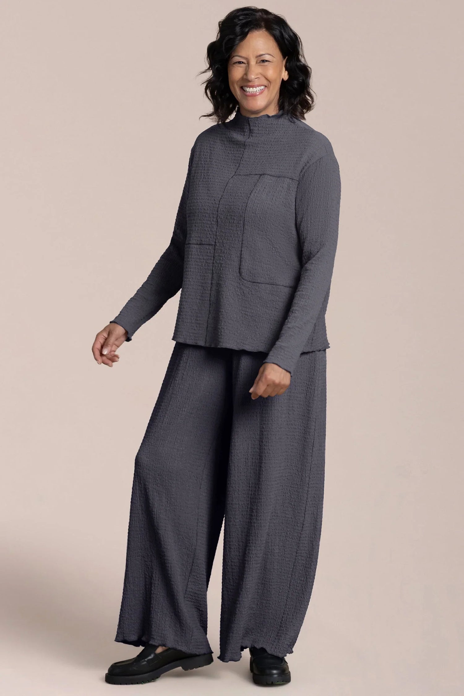 Woman wearing a gray outfit with wide-leg pants on a beige background