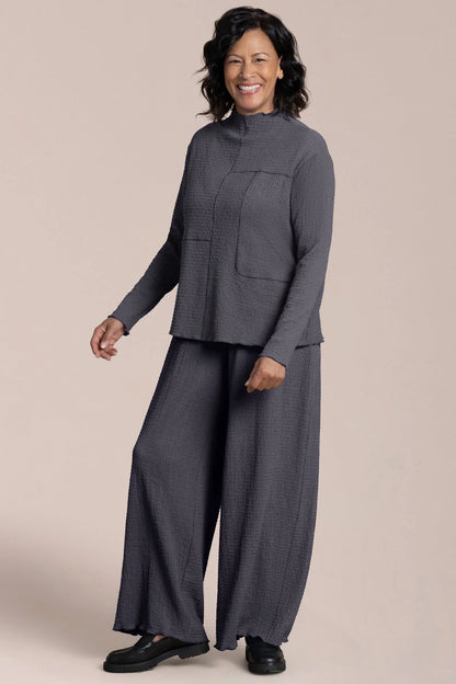 Woman wearing a gray outfit with wide-leg pants on a beige background