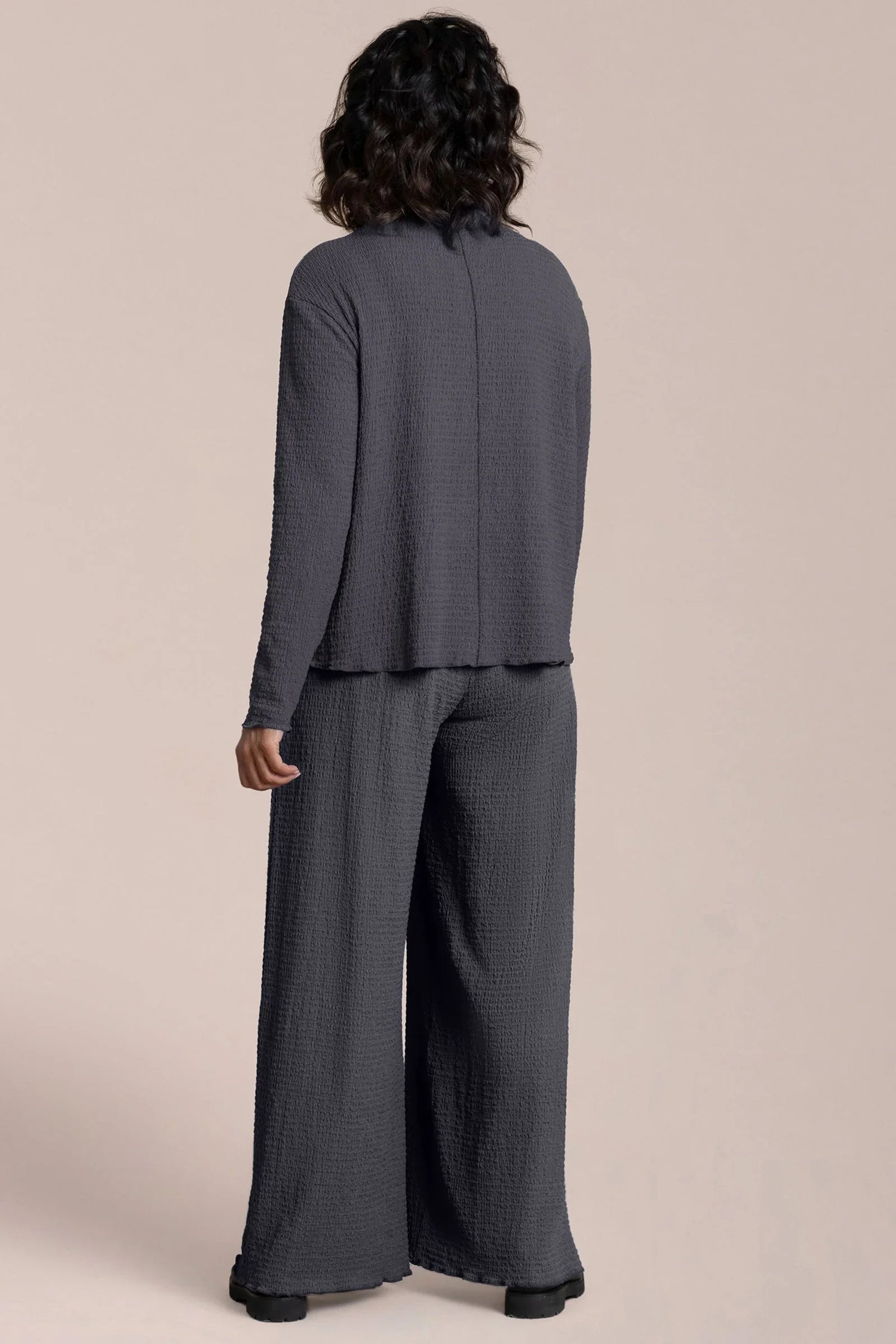 Person wearing a gray suit with wide-leg pants on a beige background