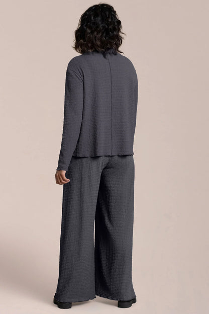 Person wearing a gray suit with wide-leg pants on a beige background