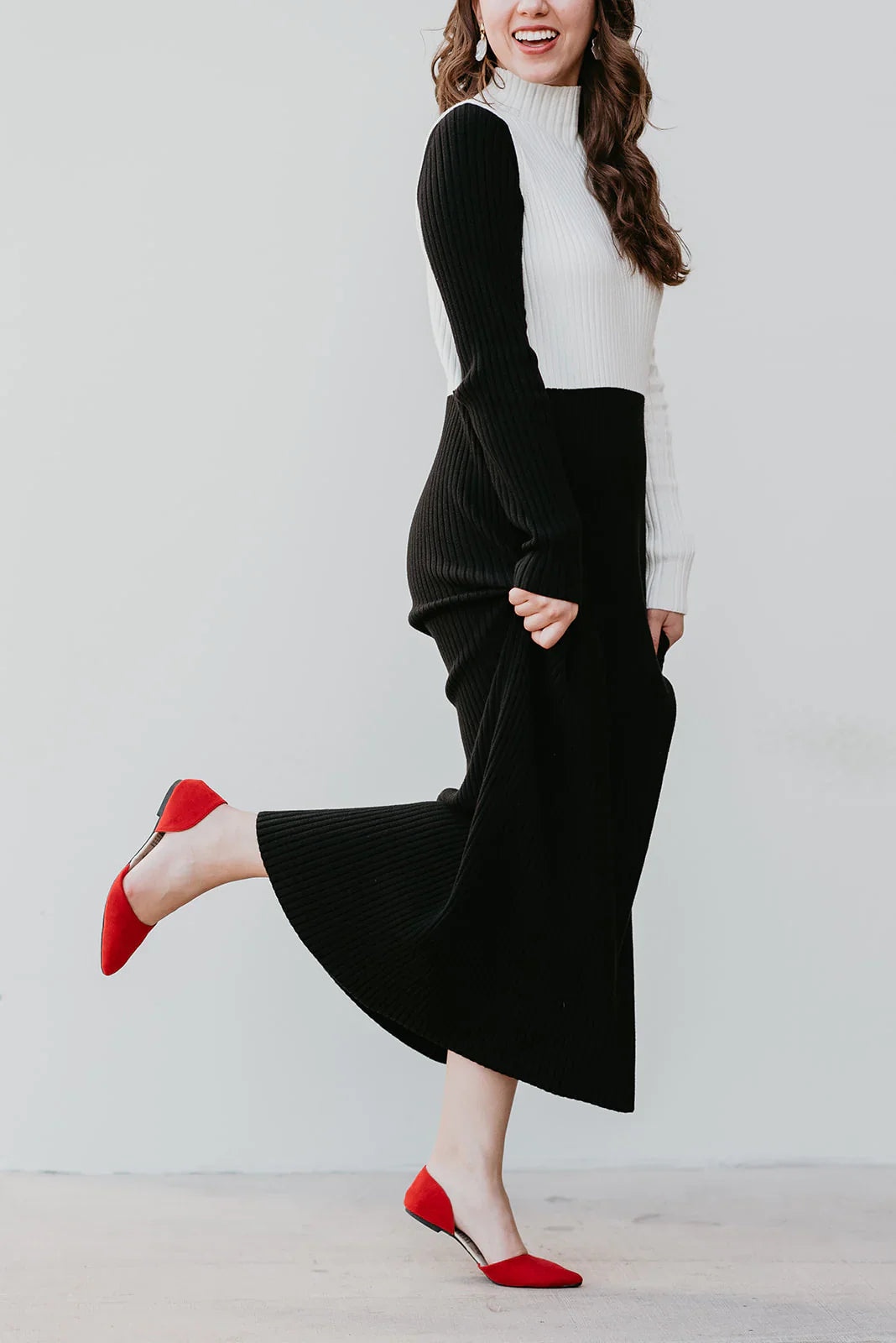 Woman wearing a black and white outfit with red shoes on a plain background