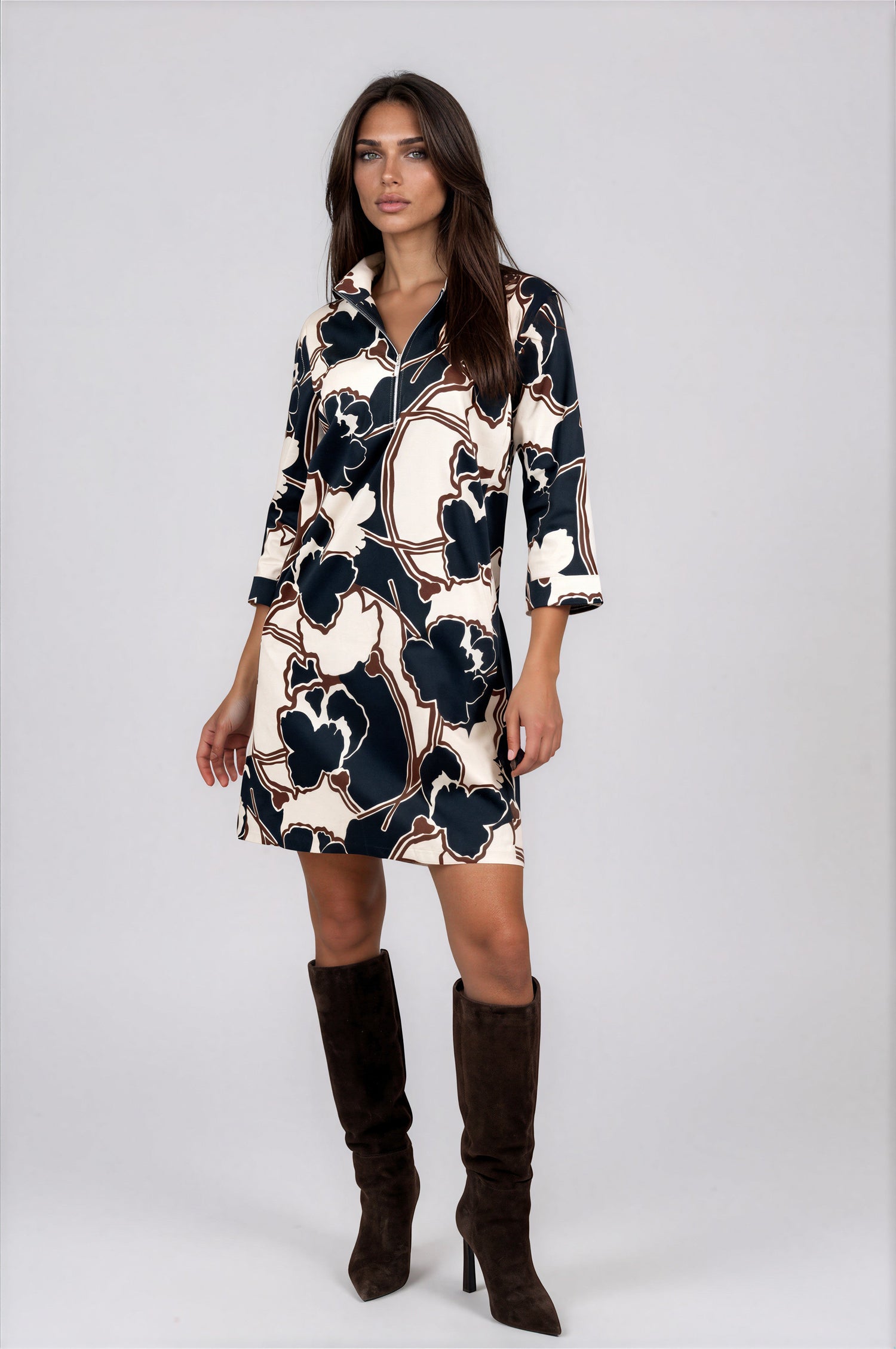 A woman modeling a knee-length collared dress with three-quarter sleeves, featuring a navy blue, cream, and brown abstract floral pattern. 