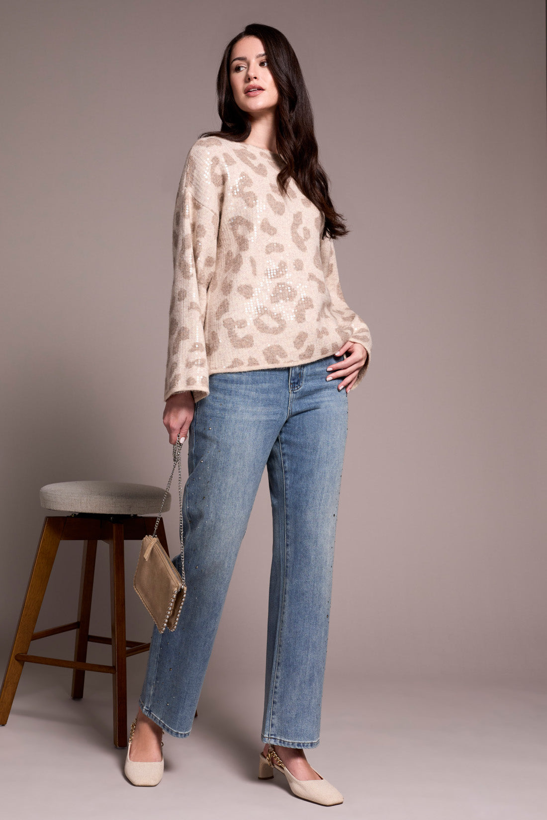 Woman wearing a patterned top and blue jeans standing against a plain background
