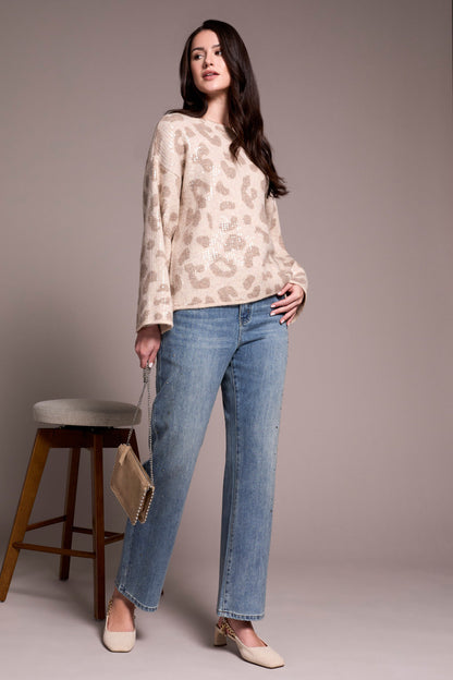 Woman wearing a patterned top and blue jeans standing against a plain background