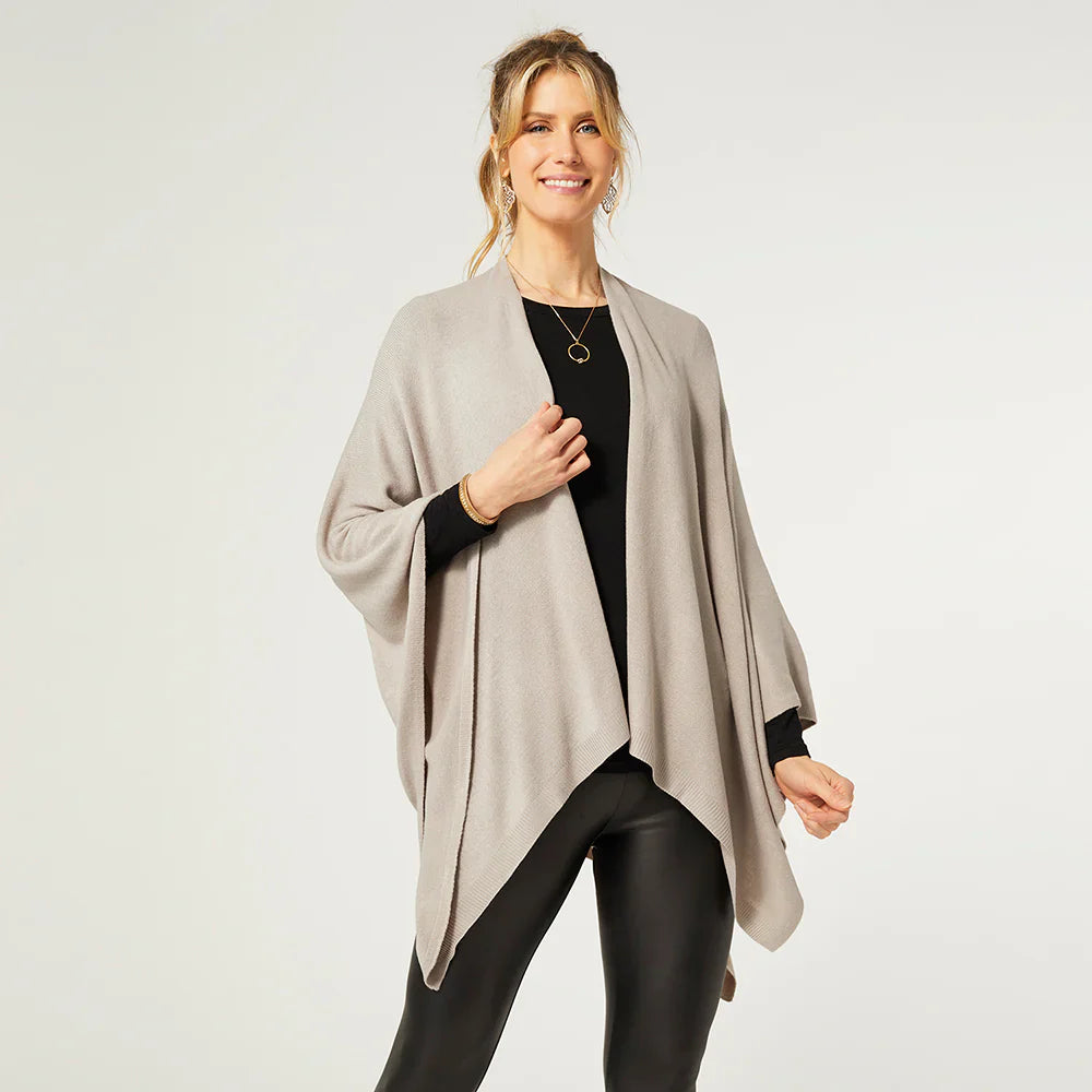 Woman wearing a silver gray poncho over a black top and leggings on a white background