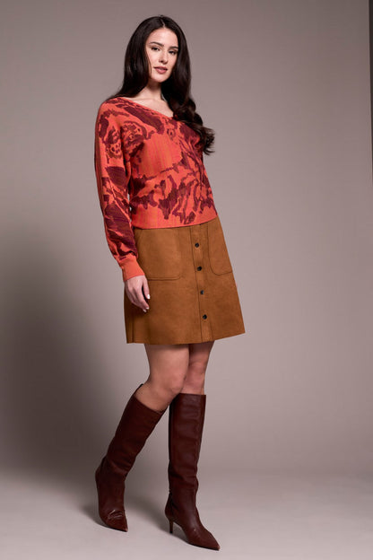 Woman wearing a red patterned sweater and brown skirt with knee-high boots on a plain background