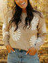 Woman wearing a beige sweater with white floral patterns in an autumn setting