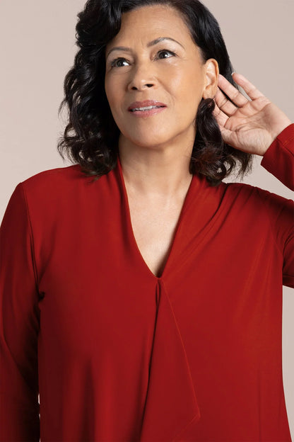 Woman in a red shirt with one hand near her ear, on a beige background