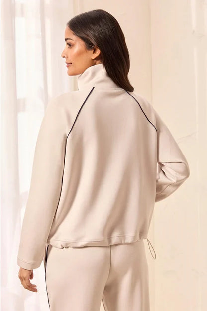 A woman modeling a matching beige tracksuit with a half-zip pullover and straight-leg pants, featuring thin black side stripes by tribal TECHNO LUX Pop Over Quarter Zip Pullover