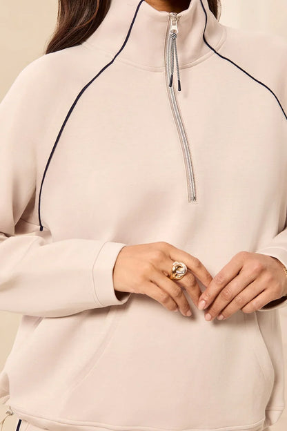 A woman modeling a matching beige tracksuit with a half-zip pullover and straight-leg pants, featuring thin black side stripes by tribal TECHNO LUX Pop Over Quarter Zip Pullover