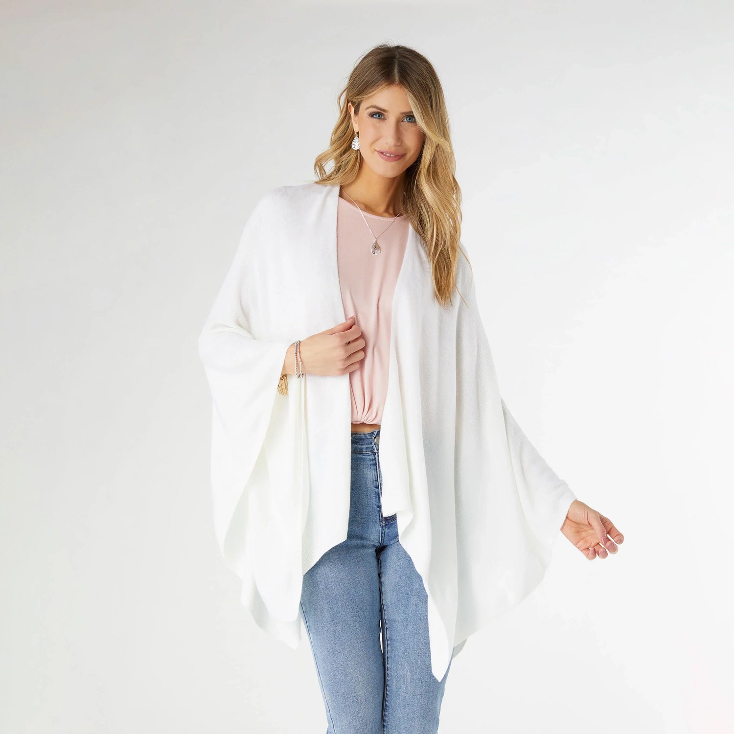 Woman wearing a white cardigan over a pink top and blue jeans on a white background