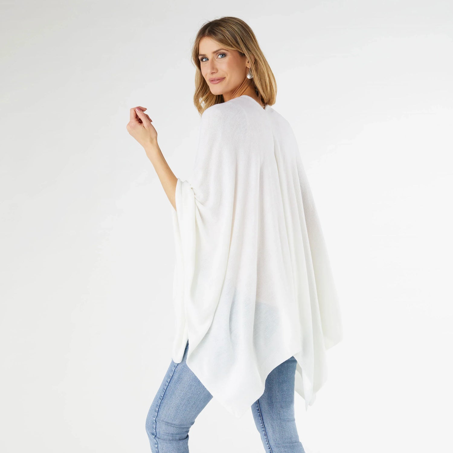 Woman wearing a white poncho over a light blue outfit on a white background