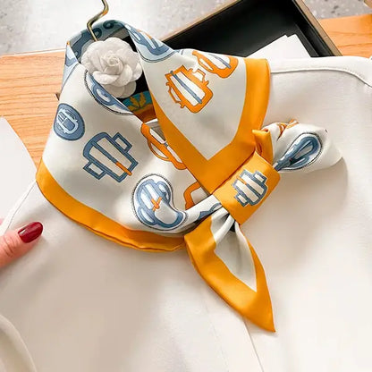 White scarf with orange border and blue geometric patterns draped over a white surface.