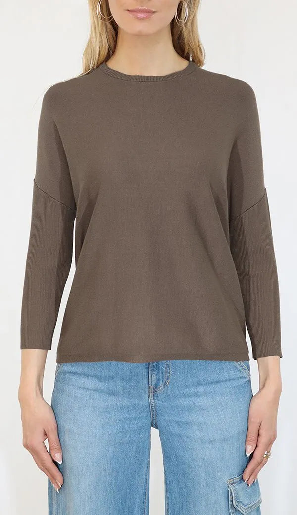 Person wearing a brown long-sleeve top and blue jeans on a white background